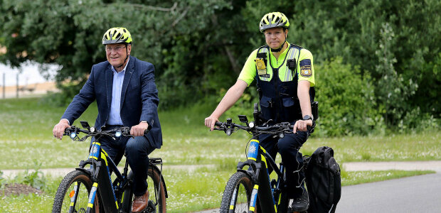 links Innenminister Joachim Herrmann und ein Polizist auf einem Fahrrad fahrend  mit Fahrradhelm auf Fahrradstraße