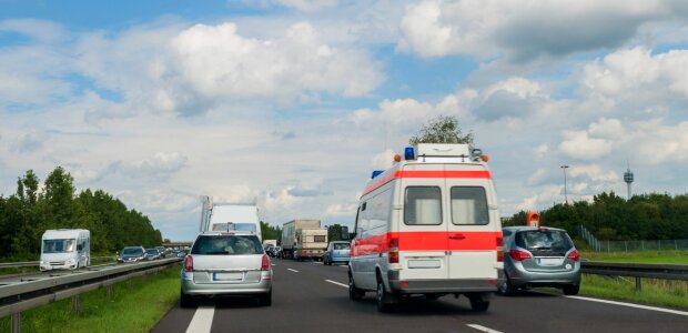 Auf dem Bild ist ein Krankenwagen zu sehen, der durch eine Rettungsgasse auf der Autobahn fährt. Links und rechts vom Rettungswagen stehen Autos.