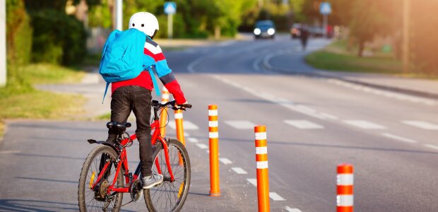 Innenminister Joachim Herrmann fordert mehr Rücksicht, Schutz und Aufmerksamkeit für Kinder im Straßenverkehr. - © AdobeStock Kind mit Rucksack auf Fahrrad kurz vor dem Überqueren einer Straße. Aus der Ferne kommt ein Auto.